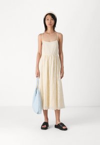 Vestido midi sin mangas de color amarillo claro, con tejido texturizado y cintura fruncida, combinado con sandalias planas negras y un bolso azul claro.