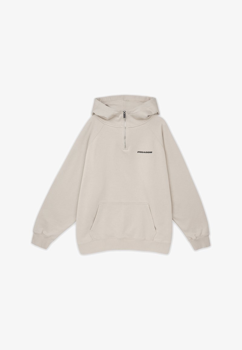 Beige huvtröja med halvmatchning och dragkedja, framficka och broderad logotyp på vänster bröst. Tyget är mjukt och strukturerat.