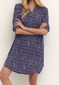 Lila Kleid mit Wellenmuster in Lavendel. Verfügt über einen Knopfkragen und kurze Ärmel. Glattes Material mit einer lockeren Passform.