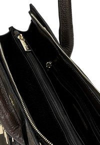 Czarna skórzana torba z fakturowanym wykończeniem, wyposażona w liczne zamykane na zamek kieszenie oraz detale w kolorze złotym. Wnętrze wyłożone czarnym materiałem.