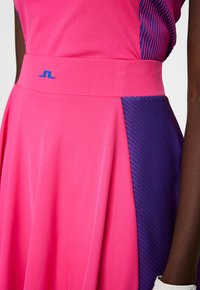 Klänning med en rosa livdel och en blårandig accent på sidan, tillverkad av ett slätt tyg med midja som sitter tajt och en utsvängd kjol.