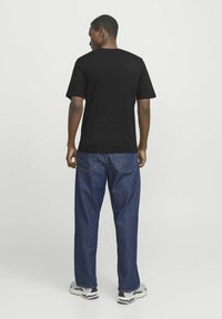 Tricou negru cu mânecă scurtă purtat cu pantaloni din denim albastru. Croială lejeră, guler rotund, țesătură simplă, fără modele sau logo-uri vizibile. Pantofi cu accente distincte.