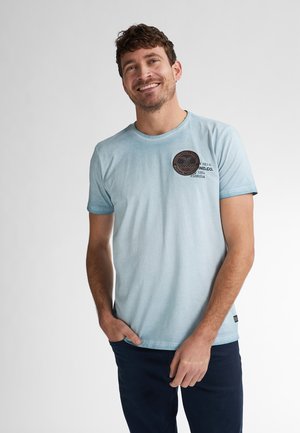 Helles blaugraues Baumwoll-T-Shirt mit kurzen Ärmeln, Rundhalsausschnitt und runder Patch-Applikation auf der Brust mit Text. Glatte Textur, lässiges Design.