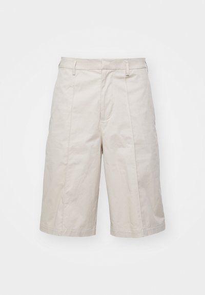 Shorts en coton beige avec une coupe droite, longueur genoux, dotés de deux poches frontales et de plis subtils pour une texture supplémentaire.