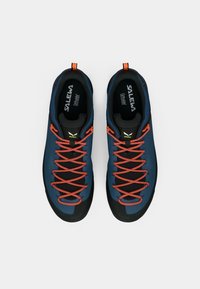 Μπλε αναρριχητικά παπούτσια με μαύρες ελαστικές σόλες, πορτοκαλί κορδόνια και υφή στην πάνω επιφάνεια. Διαθέτουν λογότυπο και βρόχους για εύκολη φόρεση.