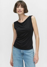 Svart ärmlös topp med ett draperat halslinje och slät textur; ihop med ljusblå denimjeans. Enkelt, figursydd design utan mönster.