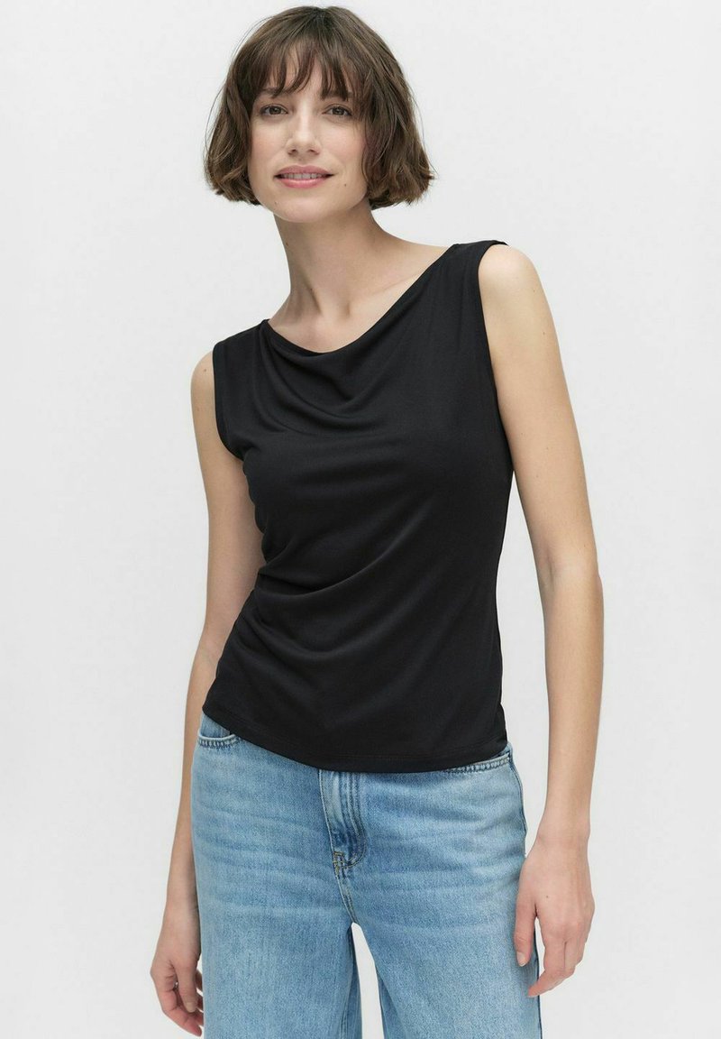 Svart ärmlös topp med ett draperat halslinje och slät textur; ihop med ljusblå denimjeans. Enkelt, figursydd design utan mönster.