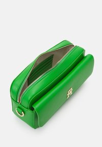 Zelená kožená obdélníková taška se zipovým uzávěrem a zlatými kovovými prvky, která má hladký povrch a vnitřní sloty na karty.