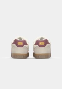 Rear view of beige and maroon sneakers with a gum sole, featuring a logo on the back and light texture details.