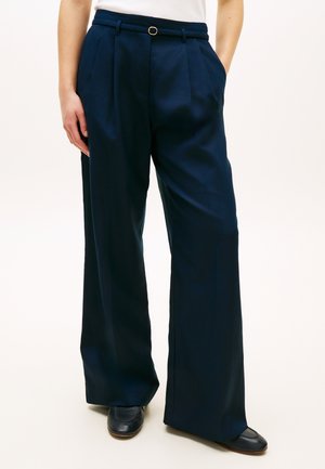 Granatowe spodnie o szerokich nogawkach z wysokim stanem, z paskiem, bocznymi kieszeniami, noszone z czarnymi butami i białym topem, widoczne od talii w dół.