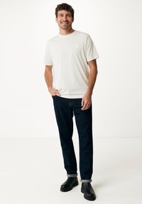 Světle béžové bavlněné tričko s malým logem na prsou, v kombinaci s tmavě modrými denimovými džíny a černými kotníkovými botami. Volný střih.