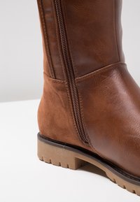 Brązowy botek ze skóry i zamszu z bocznym zamkiem błyskawicznym, teksturowaną powierzchnią oraz trwałą gumową podeszwą z bieżnikiem.