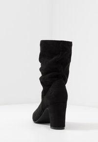 Černé semišové kotníkové boty se uvolněným designem, kulatou špičkou a masivním podpatkem. Hladká textura s bezešvým provedením a bez viditelných kovových prvků.