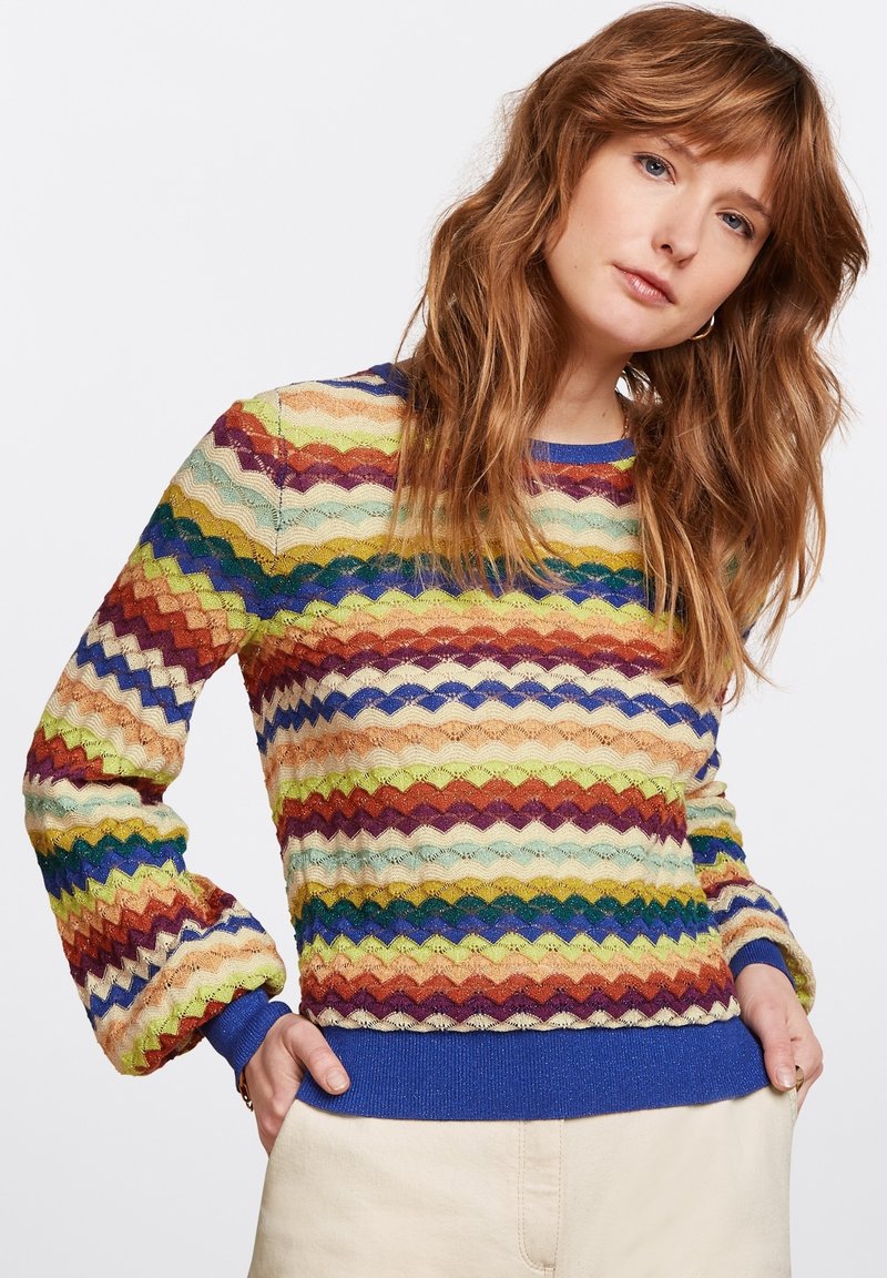 Multicolor trui met een zigzagpatroon in tinten blauw, groen, rood en goud; gebreide textuur en een effen blauwe geribde zoom.