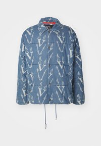 Chaqueta de denim con un diseño acolchado, que presenta un fondo azul y un patrón repetido en blanco de la letra "V". Incluye cierres a presión y dobladillo con cordón.