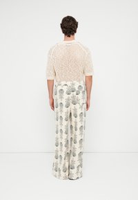 Suéter de punto crema de manga corta con tejido abierto, combinado con pantalones anchos crema con un estampado floral gris.