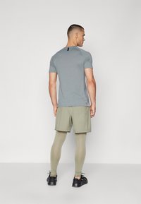 Grå kortärmad träningsskjorta med en svart detalj på baksidan, kombinerad med olivgröna shorts och matchande tajta leggings. Svarta sneakers.