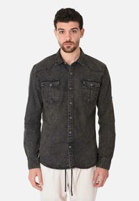 Camicia in denim scuro con chiusura a bottoni, due tasche sul petto e cuciture distintive. Presenta un colletto a punta e un orlo regolabile con cordini.