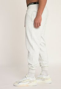 Grijze sweatpants met elastische boorden, voorzien van zijzakken en een zwarte merkband. Gekleed met witte en beige sportschoenen.