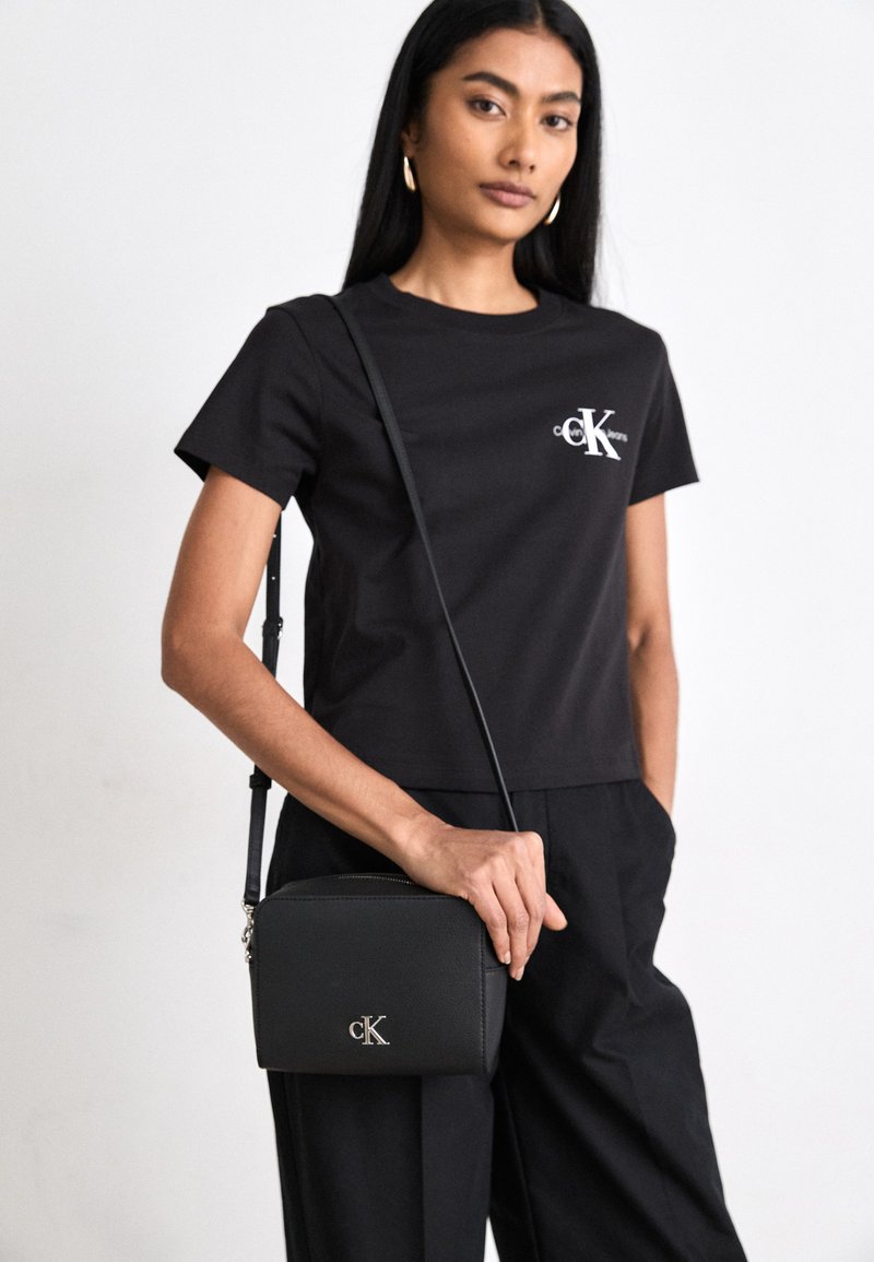 T-shirt nera a maniche corte con logo sul petto, abbinata a una borsa a tracolla nera con chiusura in argento e finitura testurizzata.