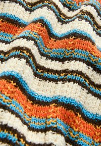 Couverture tricotée avec des rayures ondulées en crème, orange, bleu, marron et jaune ; surface texturée avec des motifs de points variés.
