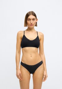 Μαύρο μπραλέτ με δαντελένιο τελείωμα και ρυθμιζόμενους ιμάντες, συνδυασμένο με μαύρο σλιπ ψηλής μέσης με μικρή λεπτομέρεια φιόγκου.