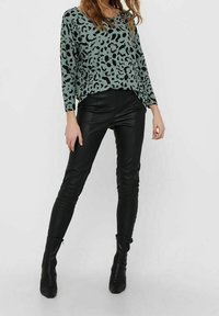 Hellblauer Leopardenmuster-Pullover, lässiger Schnitt, lange Ärmel. Enganliegende schwarze Kunstlederhosen mit Nahtdetails, knöchelhohe Stiefel.