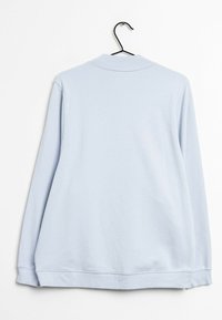 Světle modrý svetr s dlouhým rukávem pověšený na černém ramínku na bílém pozadí, zobrazený zezadu.