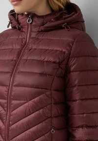Burgundská pufovaná bunda se zipem vpředu, chevronovým prošíváním, kapucí na šňůrku a stříbrnými kovovými detaily. Hladký, lehký materiál.