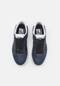 Sneakers Vans azul-marinho com cadarços pretos, interior branco e painéis em contraste. Apresenta uma textura de couro liso e sola de borracha.