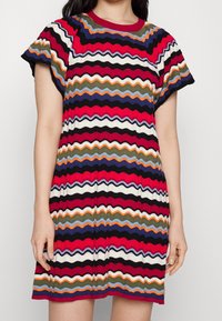 Vestido de punto colorido con un patrón de zigzag en rojo, negro, blanco, naranja, azul y verde. Mangas cortas y escote redondo.