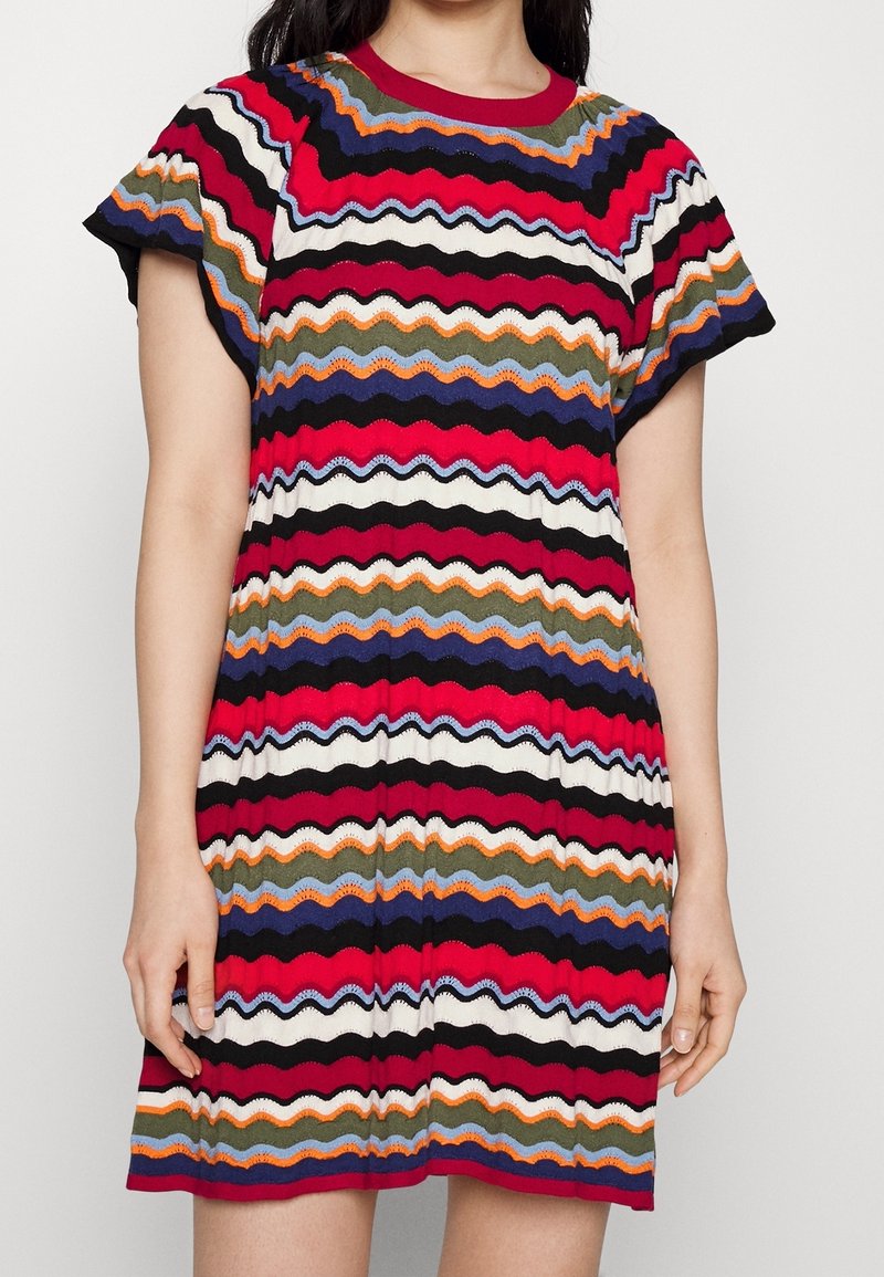 Vestido de punto colorido con un patrón de zigzag en rojo, negro, blanco, naranja, azul y verde. Mangas cortas y escote redondo.