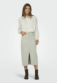 Lichtgrijze rok tot de knie met een voorkap, gecombineerd met een crèmekleurig button-up shirt. Model draagt bruine enkellaarsjes. Soepele, zachte stof.