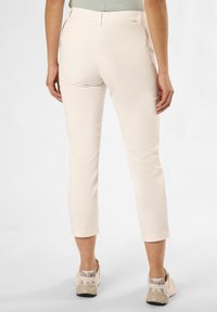 Beige cropped pants with a smooth fabric, rear pockets, and a fitted waist, paired with light-colored sneakers featuring grey accents.