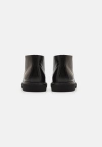 Black leather ankle boots with a smooth texture, rounded toe, and a low, sturdy rubber sole. Features minimal stitching and logo detail.