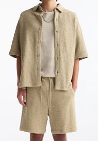 Beige texturiertes Kurzarmhemd mit Kragen, geknöpfter Vorderseite und passenden Shorts mit elastischem Bund und Kordelzug.