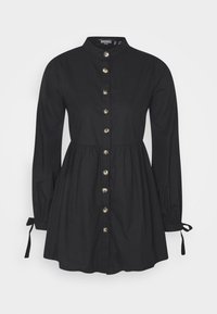 Svart knäppt klänning, långa ärmar med knytdetaljer, midjan är åtdragen, tillverkad av slätt tyg. Har guldfärgade knappar fram.