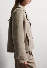 Chaqueta de lana beige de doble botonadura con solapas con muescas, bolsillos laterales y detalles en botones marrones. Tejido texturizado con un ajuste a medida.