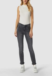 Graue Slim-Fit-Jeans mit hoher Taille und umgeschlagenen Säumen, kombiniert mit einem eng anliegenden, ärmellosen weißen Shirt und hellen Sneakers. Sanfte, Denim-Textur.