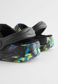 Sabots noirs avec une sangle texturée, ornés d'un motif abstrait multicolore dans des teintes de vert, bleu et violet sur la semelle. Doublure douce et pelucheuse.