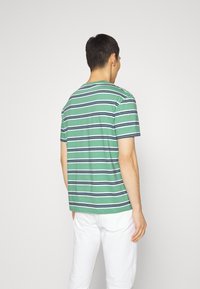 Zielona koszulka w paski z granatowymi i białymi poziomymi liniami, wykonana z bawełny, krótki rękaw, okrągły dekolt. Zaprezentowany widok z tylu.