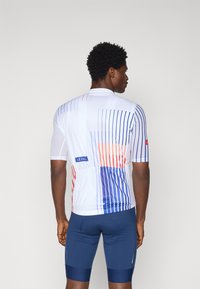 Short-sleeved cycling jersey featuring a white base with blue vertical stripes and red accents. Textured fabric with mesh details for breathability.