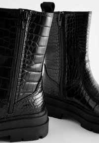 Schwarze ankle boots aus glänzendem, krokodilpräge Material, mit Vorderreißverschluss, strukturiertem Sohle und robustem Design.