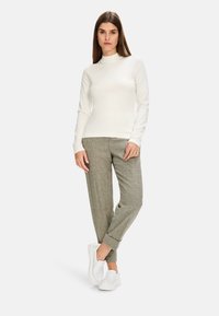 Weißes langärmeliges Oberteil mit Stehkragen; graue Karohosen mit schmal zulaufendem Bein; weiße Slipper; glatte Texturen und neutrale Farben.