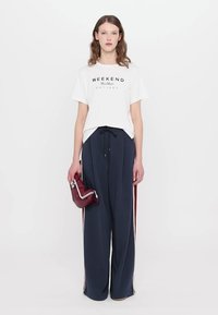 Weißes Baumwoll-T-Shirt mit "WEEKEND MaxMara"-Druck, kombiniert mit navyblauen weit geschnittenen Hosen mit roten Seitenstreifen und einer burgunderfarbenen Handtasche.