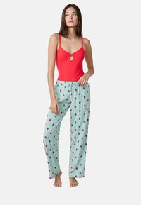 Body rosso senza maniche con dettaglio a chiave, abbinato a pantaloni del pigiama a righe blu chiaro con motivi di fragole rosse.