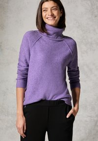 Lila Strickpullover mit einem Rollkragen, gerippten Bündchen und einem entspannten Schnitt. Kombiniert mit schwarzen Hosen, die Taschen und eine glatte Textur haben.