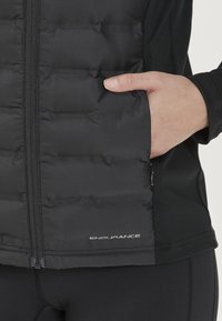 Sort pufferjakke med lynlås foran, med en quiltet design, sidelommer og et "ENDURANCE" logo i kanten. Glat stoftekstur.