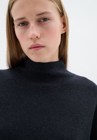 Mörkgrå, mjukstickad polotröja med en figurnära design och slät textur, med hög krage och minimala detaljer.