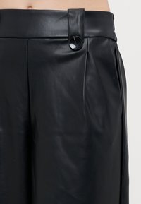 Black leather trousers feature a smooth texture, wide leg design, and a high waistband with a large circular button detail on the front.